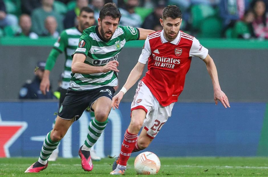 Cầu thủ Sporting trong trang phục áo kẻ sọc Xanh-Trắng đang theo bóng với một cầu thủ của Arsenal. 